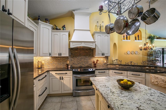 kitchen featuring white cabinets, decorative backsplash, dark stone countertops, appliances with stainless steel finishes, and light tile patterned flooring