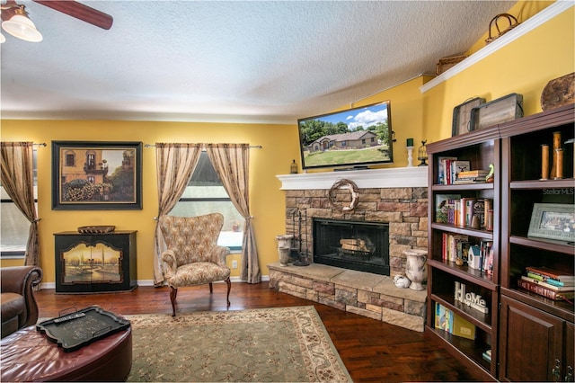 living room featuring hardwood / wood-style floors, ceiling fan, a stone fireplace, and a textured ceiling