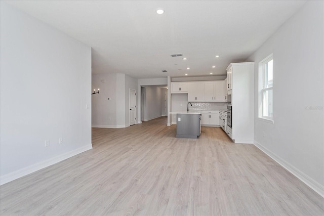 kitchen featuring stainless steel appliances, white cabinets, an island with sink, and light hardwood / wood-style floors