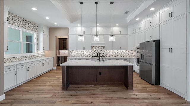 kitchen featuring black fridge, pendant lighting, a center island with sink, white cabinets, and light stone counters