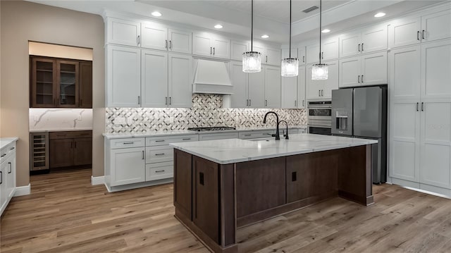 kitchen featuring custom exhaust hood, a center island with sink, stainless steel appliances, beverage cooler, and sink