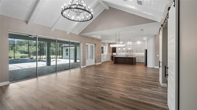 unfurnished living room featuring dark hardwood / wood-style flooring, beamed ceiling, a chandelier, high vaulted ceiling, and a barn door