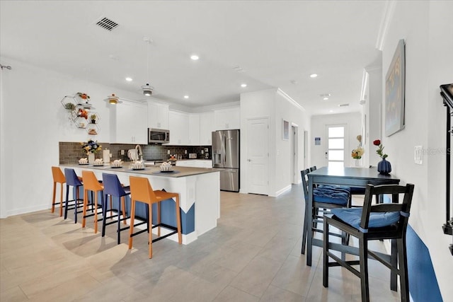 kitchen with backsplash, a kitchen bar, appliances with stainless steel finishes, a peninsula, and white cabinetry
