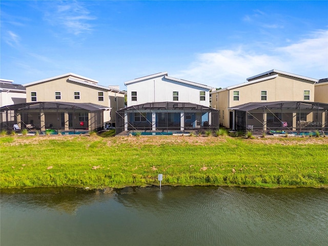 rear view of house featuring a lawn, glass enclosure, a water view, and a swimming pool