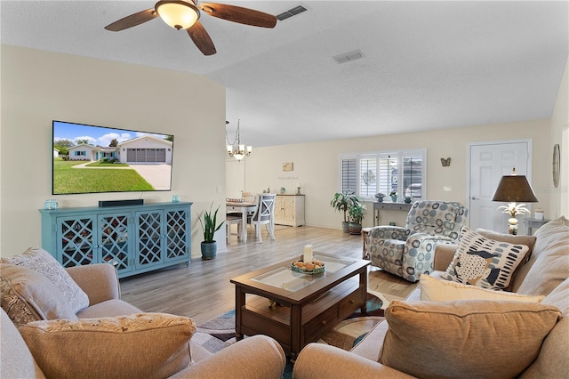 living room with ceiling fan with notable chandelier, vaulted ceiling, and light hardwood / wood-style flooring