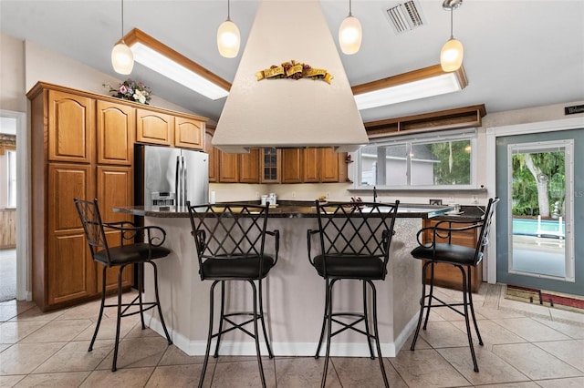 kitchen with a kitchen breakfast bar, light tile floors, a center island, lofted ceiling, and stainless steel fridge with ice dispenser