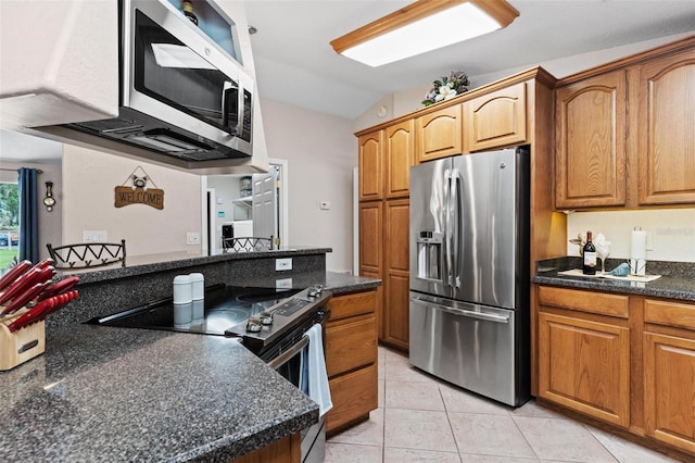 kitchen featuring vaulted ceiling, appliances with stainless steel finishes, dark stone counters, and light tile floors