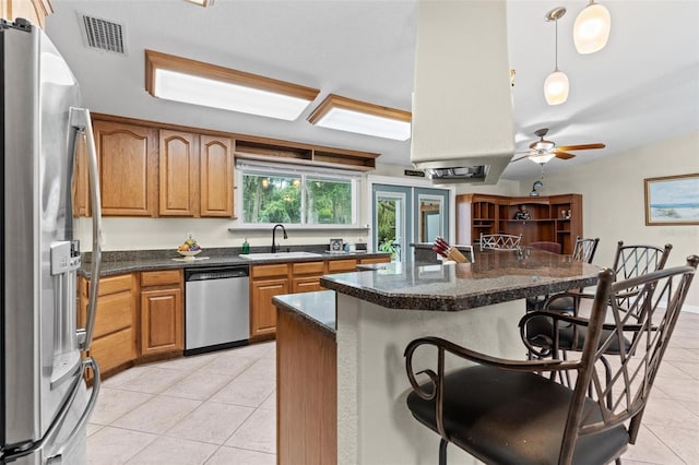 kitchen featuring stainless steel appliances, light tile floors, pendant lighting, ceiling fan, and a kitchen bar