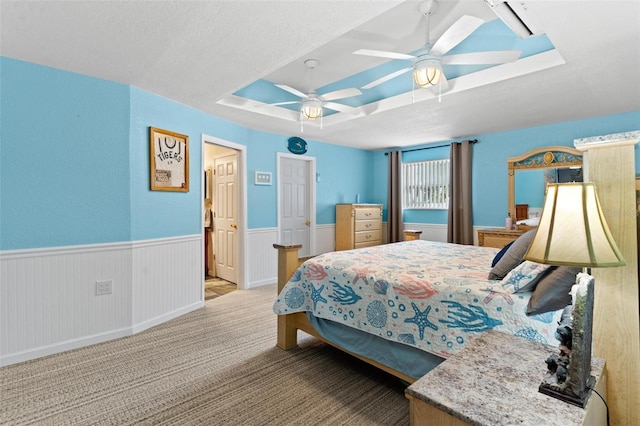 bedroom featuring a raised ceiling, carpet, ceiling fan, and a textured ceiling