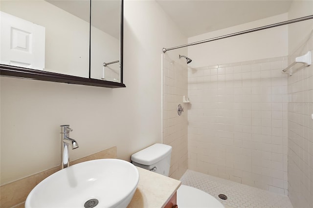 bathroom featuring a tile shower, vanity, and toilet