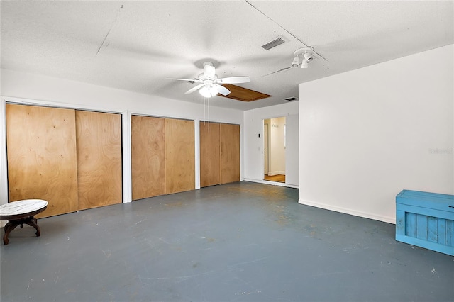 unfurnished bedroom with ceiling fan, a textured ceiling, and two closets