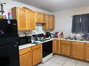 kitchen with black fridge, light tile patterned floors, sink, and white range