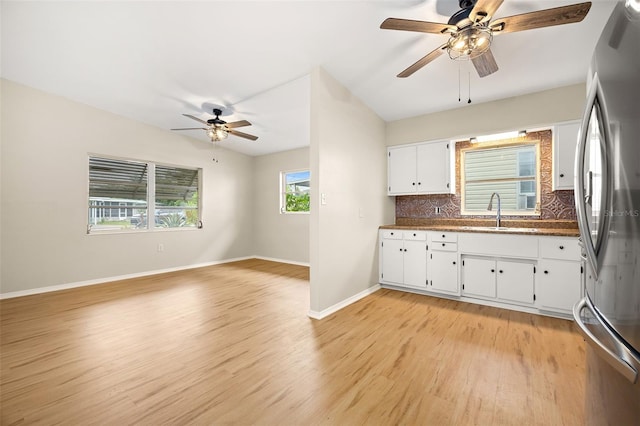 kitchen with stainless steel refrigerator, white cabinetry, sink, backsplash, and light hardwood / wood-style floors