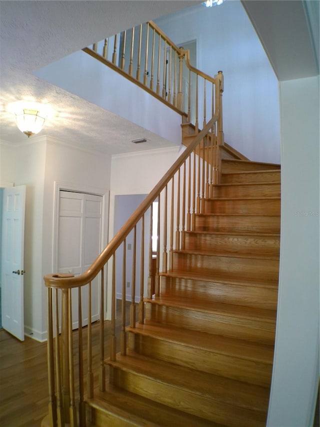 staircase with hardwood / wood-style flooring, ornamental molding, and a textured ceiling