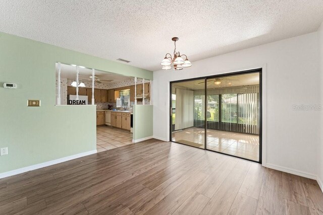 empty room featuring a textured ceiling, a chandelier, and light hardwood / wood-style flooring