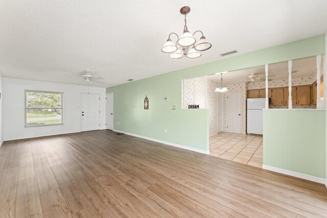 unfurnished living room with ceiling fan with notable chandelier, light hardwood / wood-style flooring, and a textured ceiling