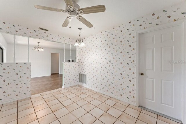 tiled spare room with ceiling fan with notable chandelier