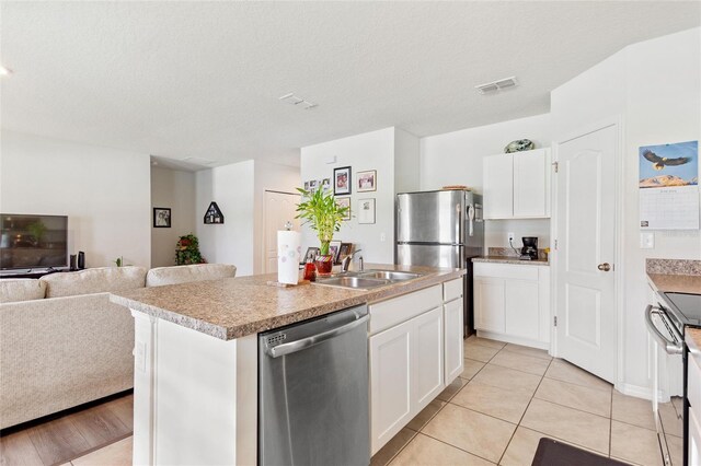 kitchen with stainless steel appliances, a center island with sink, light tile floors, sink, and white cabinetry