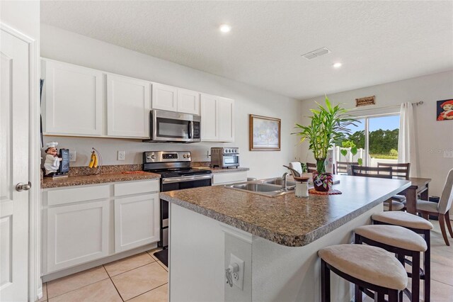 kitchen with stainless steel appliances, a kitchen island with sink, white cabinetry, sink, and light tile floors