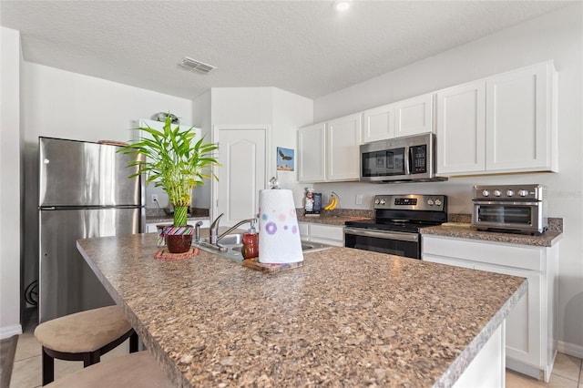 kitchen featuring stainless steel appliances, white cabinets, and an island with sink