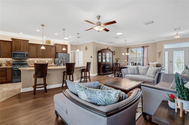 living room featuring wood-type flooring, ornamental molding, and ceiling fan with notable chandelier