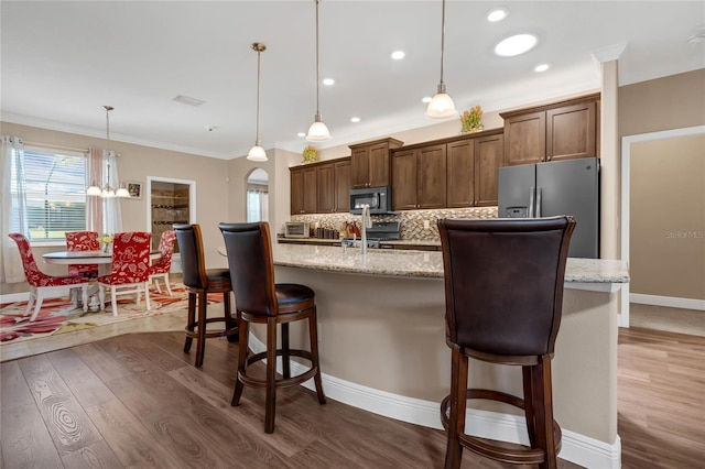 kitchen featuring dark hardwood / wood-style floors, stainless steel appliances, backsplash, hanging light fixtures, and a breakfast bar