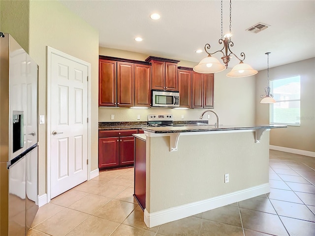 kitchen with a kitchen bar, appliances with stainless steel finishes, a center island with sink, and hanging light fixtures