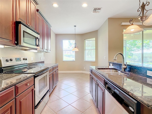 kitchen featuring hanging light fixtures, sink, dark stone countertops, light tile patterned floors, and appliances with stainless steel finishes