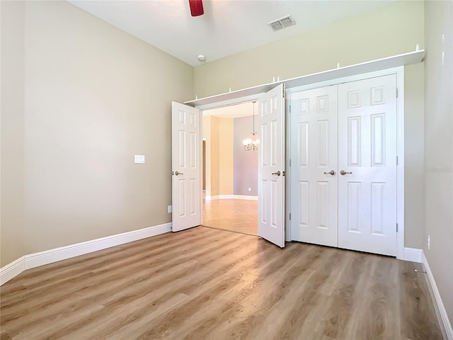 unfurnished bedroom featuring ceiling fan with notable chandelier, wood-type flooring, and a closet