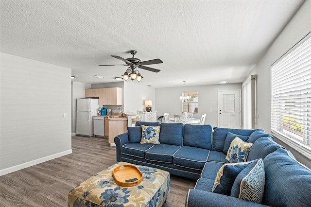 living room with wood-type flooring, ceiling fan with notable chandelier, and sink