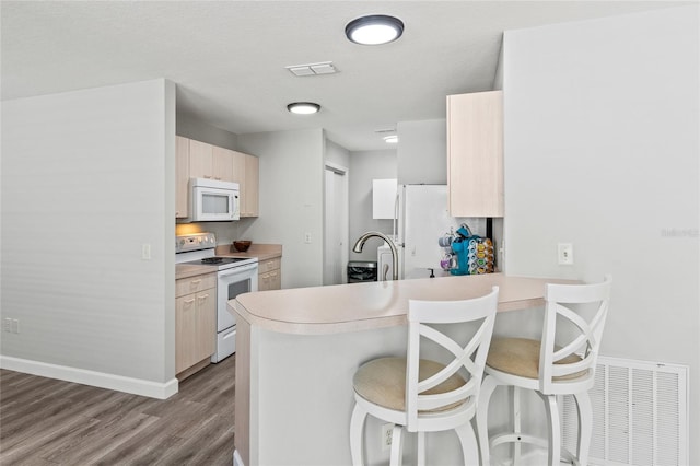 kitchen with kitchen peninsula, a breakfast bar, white appliances, sink, and light hardwood / wood-style flooring