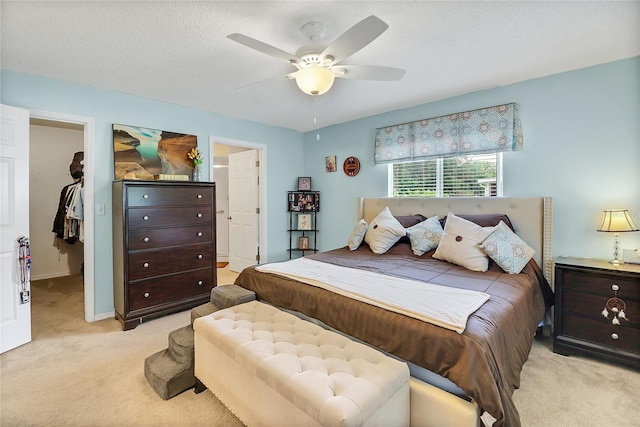 carpeted bedroom with a walk in closet, ceiling fan, a closet, and a textured ceiling