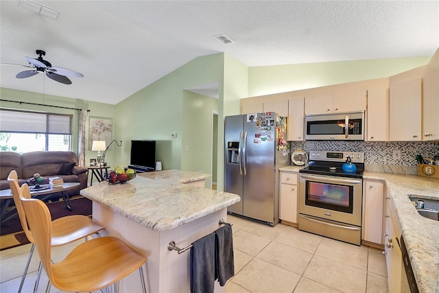 kitchen with vaulted ceiling, ceiling fan, light tile patterned floors, appliances with stainless steel finishes, and a kitchen bar