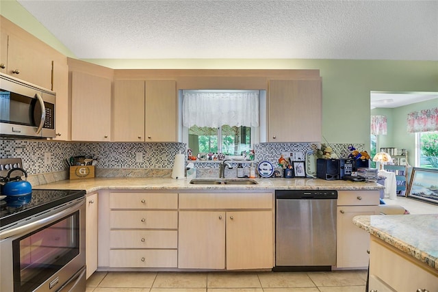 kitchen with appliances with stainless steel finishes, light brown cabinets, light tile patterned floors, and sink