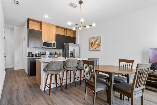 kitchen featuring light hardwood / wood-style floors, a breakfast bar, appliances with stainless steel finishes, tasteful backsplash, and decorative light fixtures