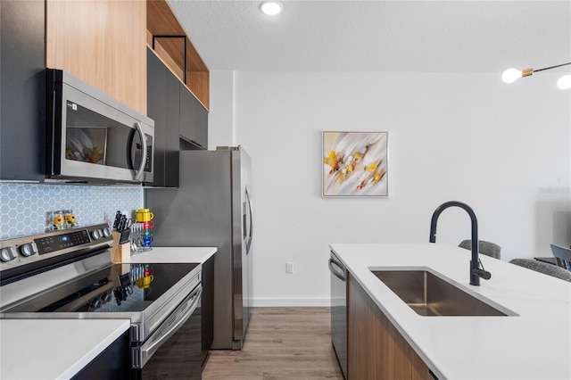 kitchen with light hardwood / wood-style floors, a textured ceiling, sink, backsplash, and appliances with stainless steel finishes