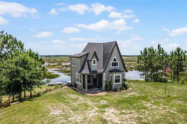 back of house featuring a rural view, a lawn, and a water view