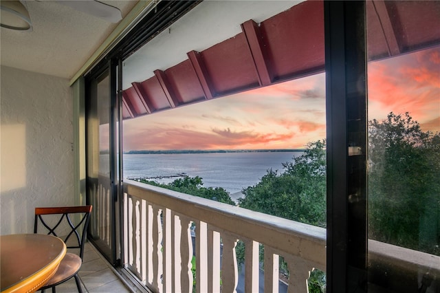 balcony at dusk featuring a water view