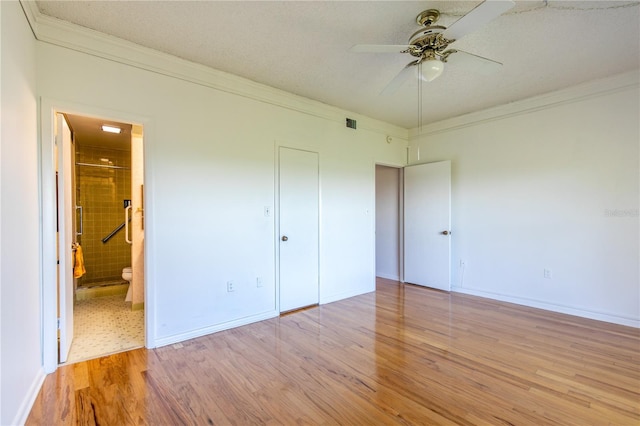 unfurnished bedroom featuring ensuite bathroom, a textured ceiling, light wood-type flooring, ornamental molding, and ceiling fan