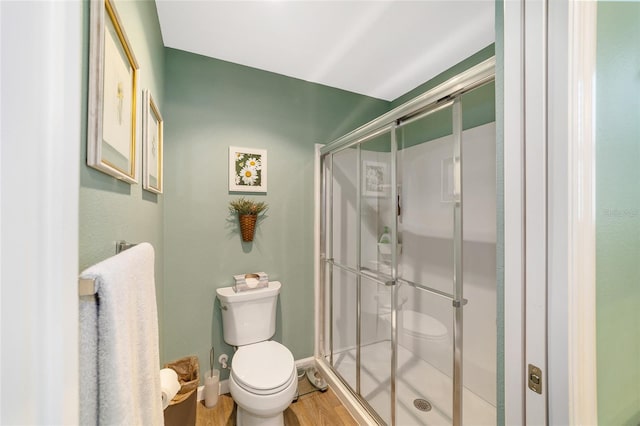 bathroom with hardwood / wood-style flooring, toilet, and a shower with shower door