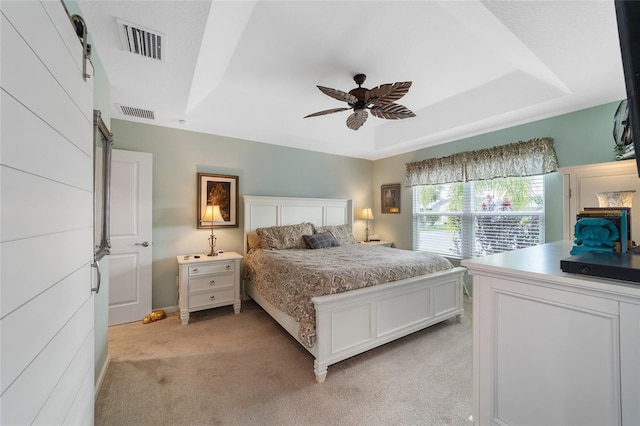 carpeted bedroom featuring a barn door, a tray ceiling, and ceiling fan