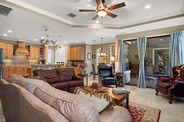 tiled living room with crown molding, a raised ceiling, and ceiling fan with notable chandelier