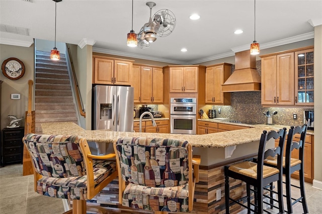 kitchen featuring appliances with stainless steel finishes, decorative light fixtures, a breakfast bar area, and custom exhaust hood