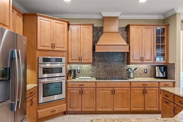 kitchen with light stone counters, decorative backsplash, stainless steel appliances, and custom range hood