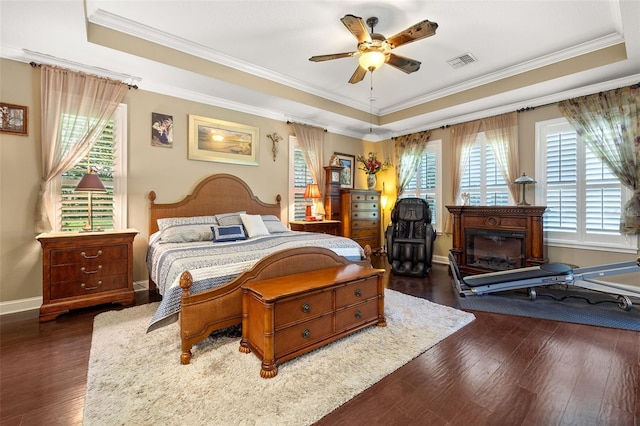 bedroom with crown molding, a tray ceiling, dark wood-type flooring, and ceiling fan