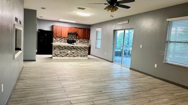 kitchen featuring black fridge, light hardwood / wood-style flooring, decorative backsplash, and ceiling fan