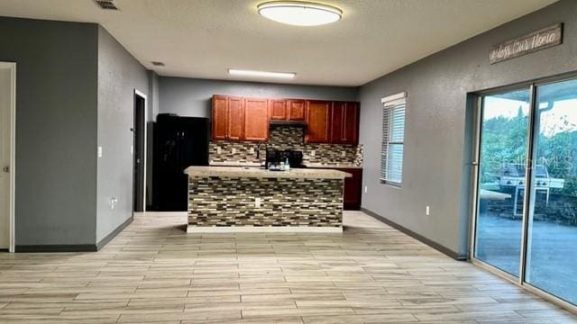 kitchen featuring plenty of natural light, tasteful backsplash, a center island, and black refrigerator