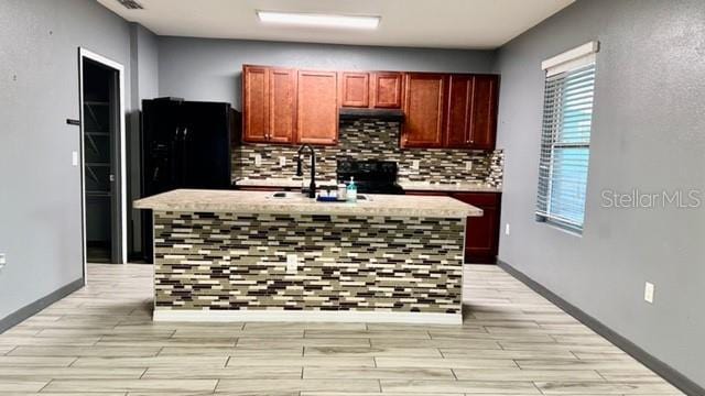 kitchen with sink, light hardwood / wood-style flooring, a kitchen island with sink, and tasteful backsplash