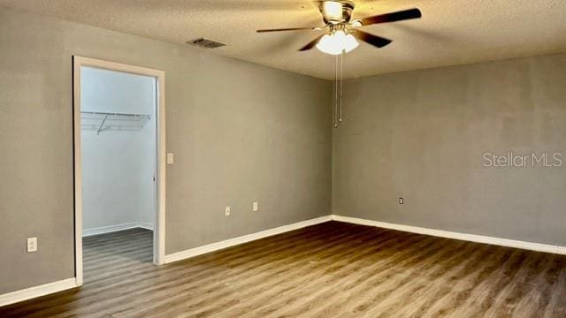 unfurnished bedroom with wood-type flooring, ceiling fan, a textured ceiling, a spacious closet, and a closet