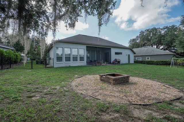 rear view of property with a lawn, a sunroom, and a fire pit